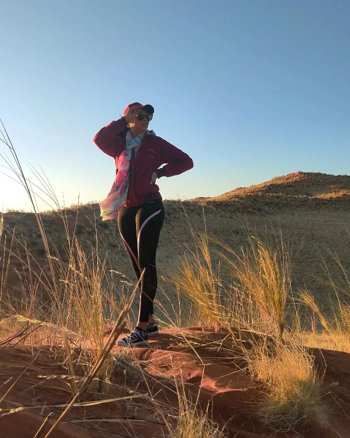 Stephanie standing among sunlit grass and red rock in the Namib Dunes
